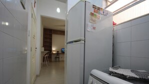 Cozinha compacta com geladeira, forno e uma pequena área de refeições visível ao fundo.