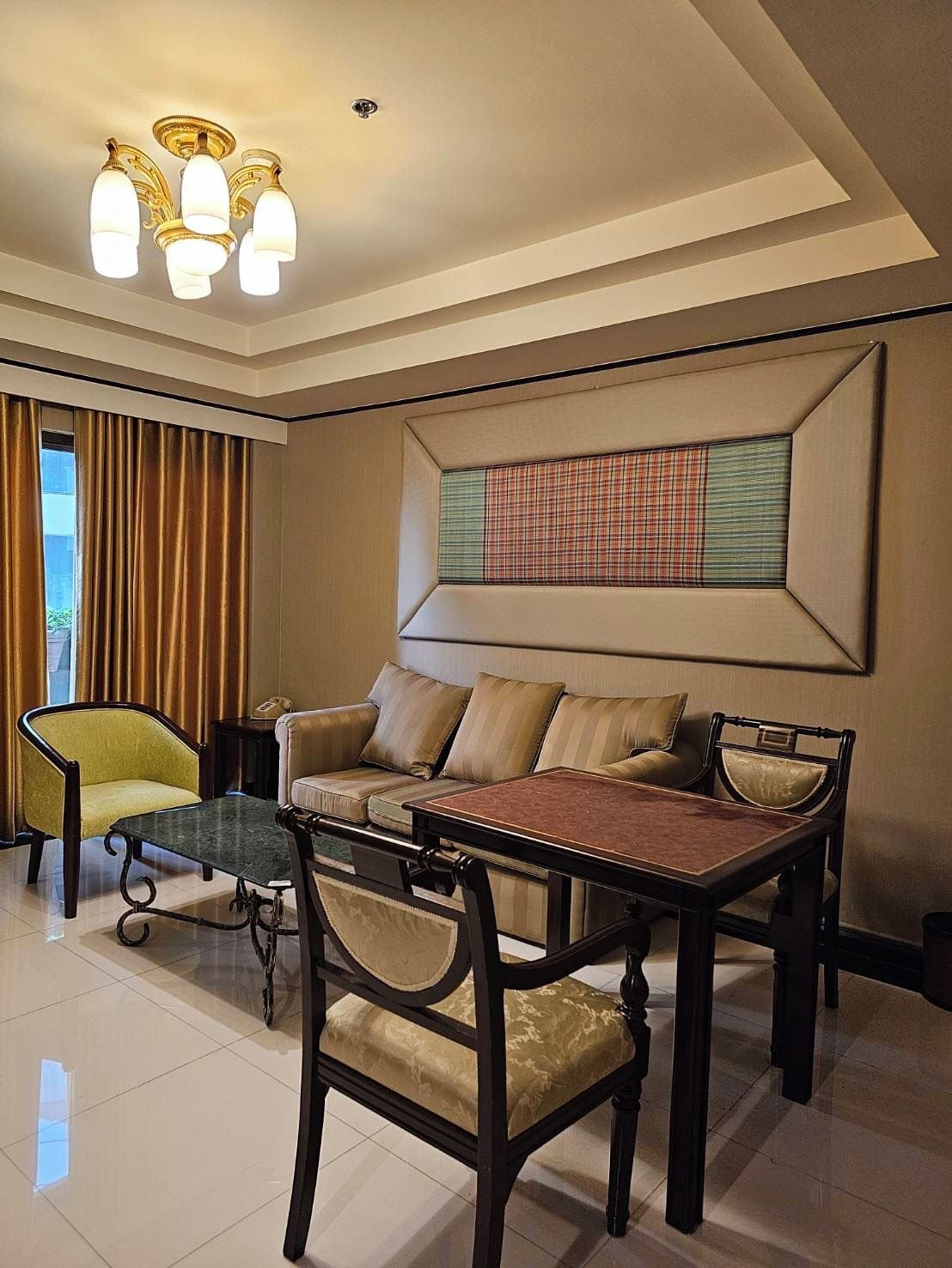 A hotel room with a sofa set, a dining table, and a chandelier.