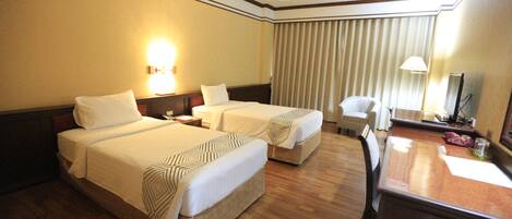 A hotel room with two beds, a desk, a chair, a lamp, and a window with curtains.
