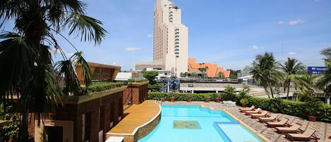 Área de piscina de hotel com uma piscina grande, espreguiçadeiras e palmeiras.