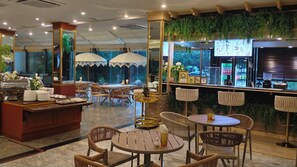 A restaurant with round tables, chairs, a buffet area, and a bar with a menu display. - Kosa Hotel & Shopping Mall (Khon Kaen)