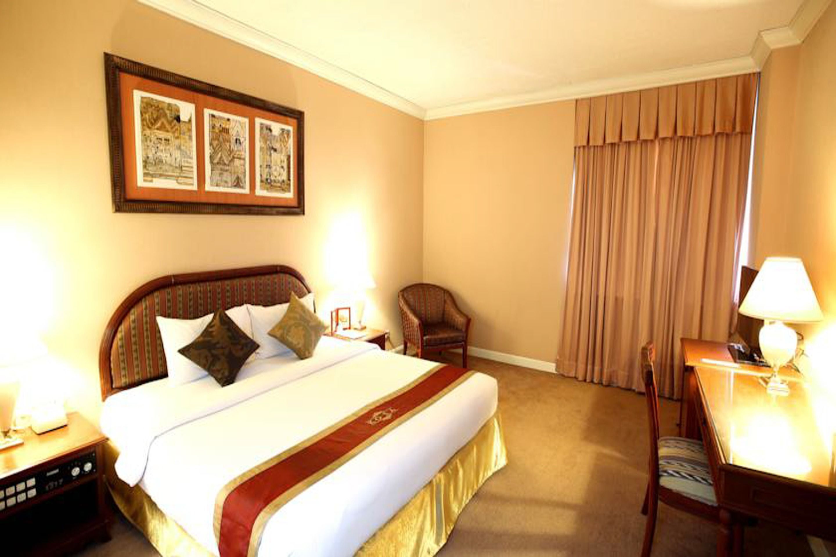 A hotel room with a large bed, a desk, a chair, and a window with curtains.