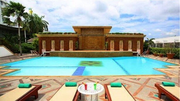 Una piscina con sillas de descanso y un edificio decorativo al fondo.