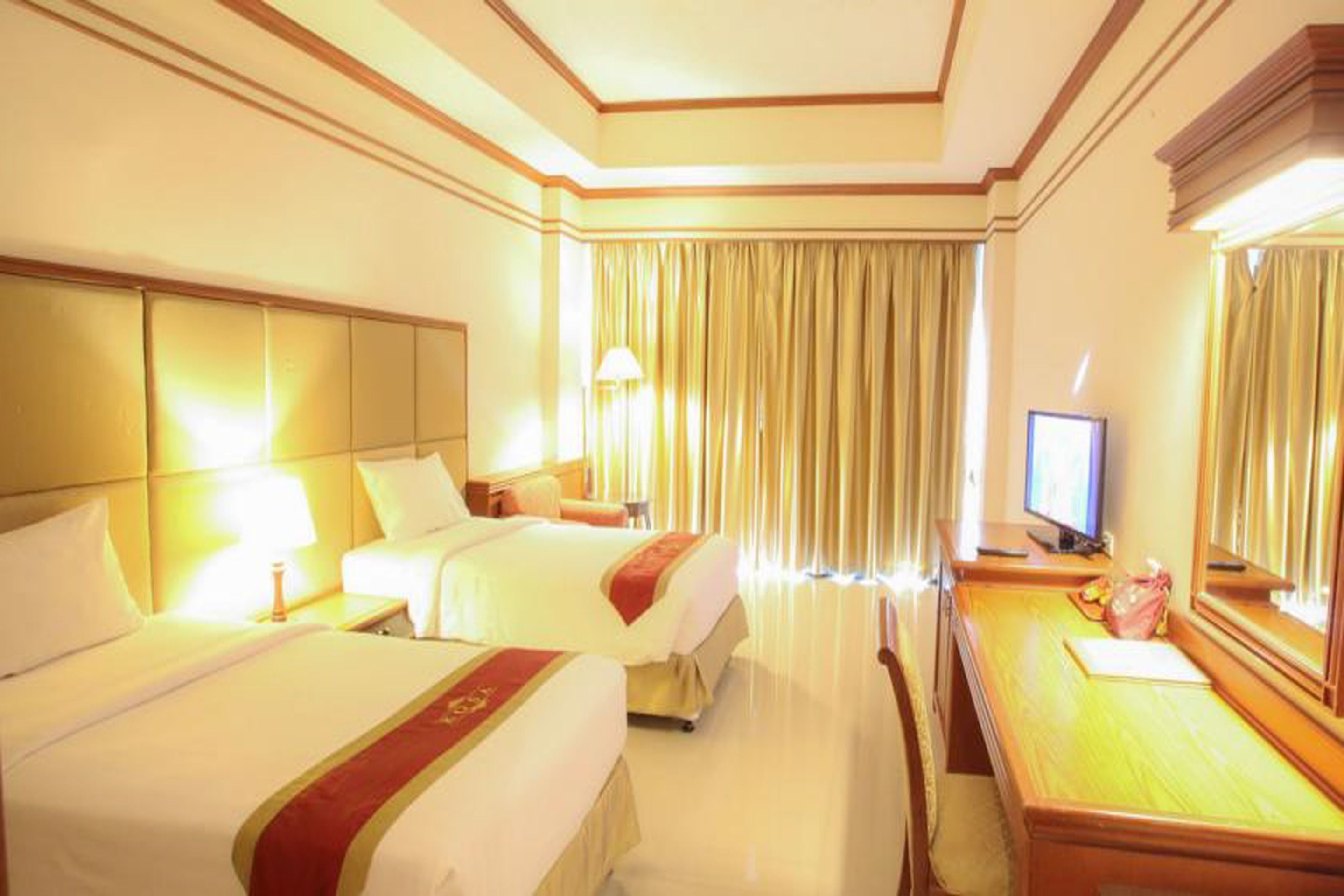 Une chambre d’hôtel avec deux lits, un bureau, une chaise, une télévision et une grande fenêtre avec des rideaux.