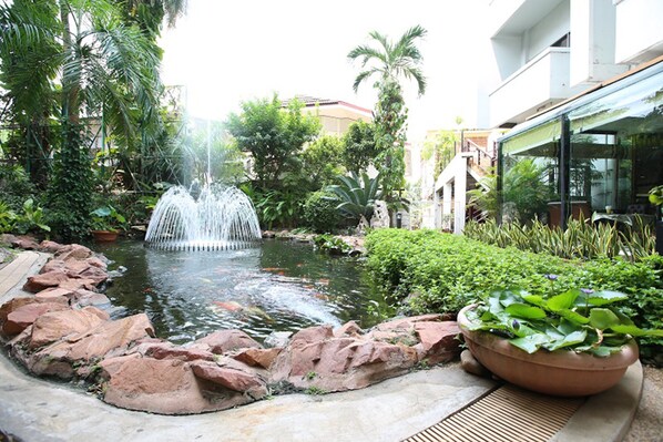 Un jardí tranquil amb una font al centre, envoltat de roques i vegetació abundant.