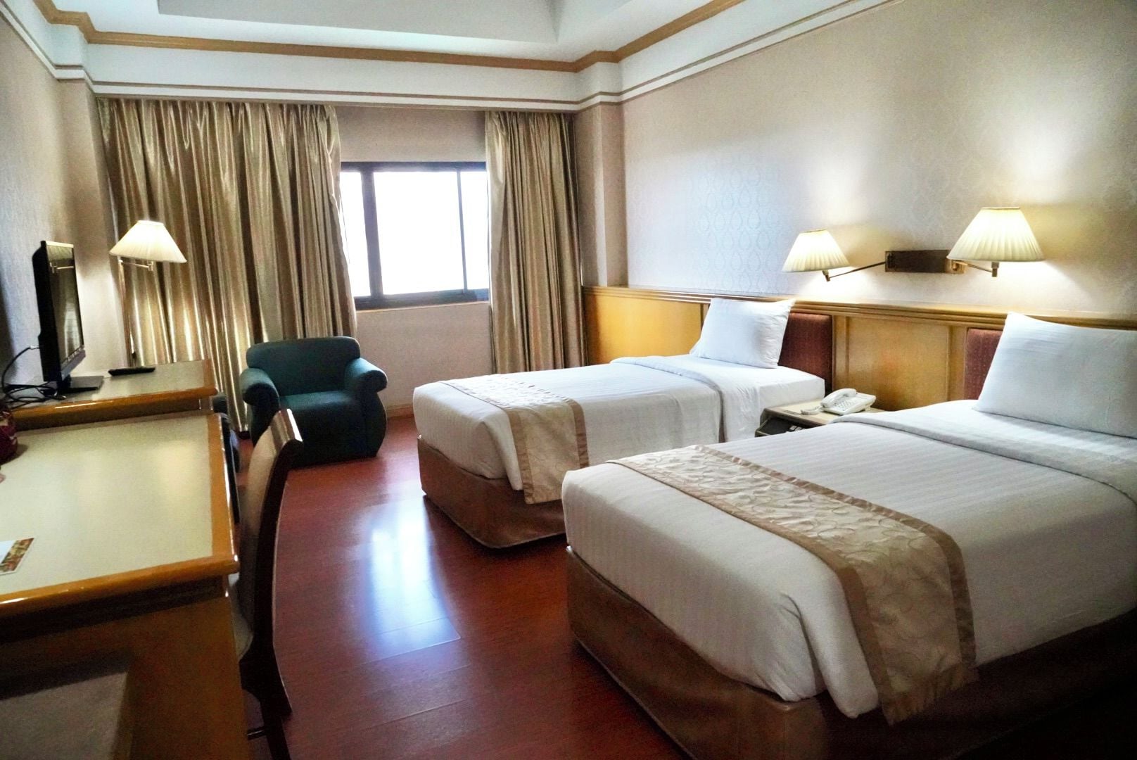 A hotel room with two beds, a desk, a chair, and a window with curtains.