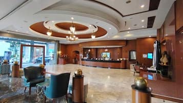 A hotel lobby with a reception desk, seating area, and a large window overlooking the street.