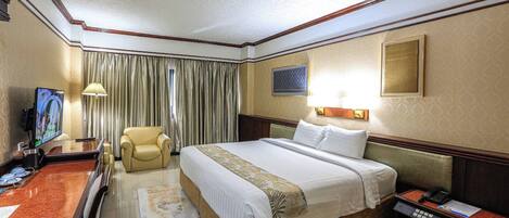 Una habitación de hotel con cama, escritorio con televisor, silla y mesita de noche con teléfono.