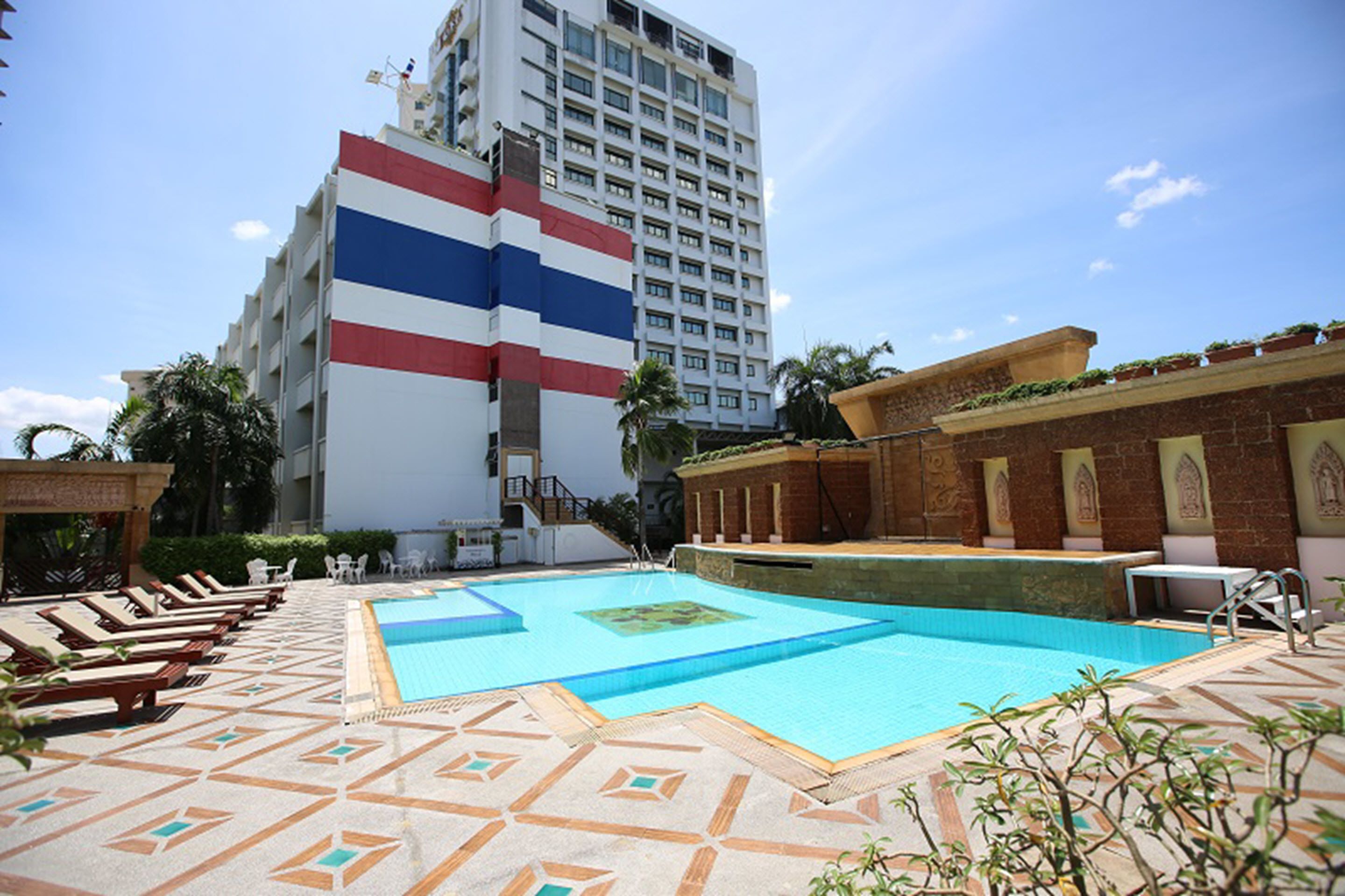A hotel pool area with lounge chairs, a pool, and a building with a flag design.