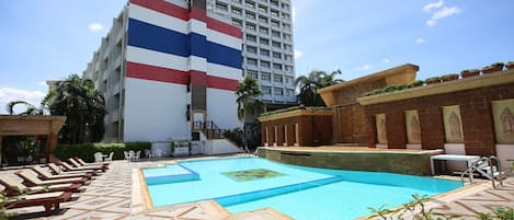 Zona de piscina de hotel con sillas de descanso, una piscina y un edificio con diseño de bandera.