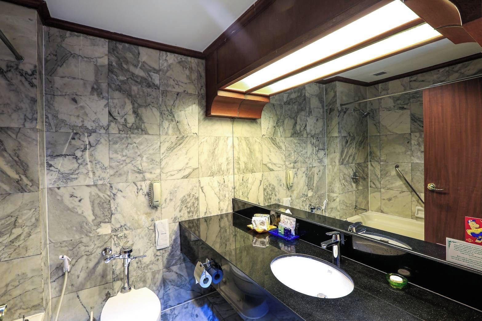 A bathroom with marble walls, a black countertop, a white sink, a large mirror, and a shower area.