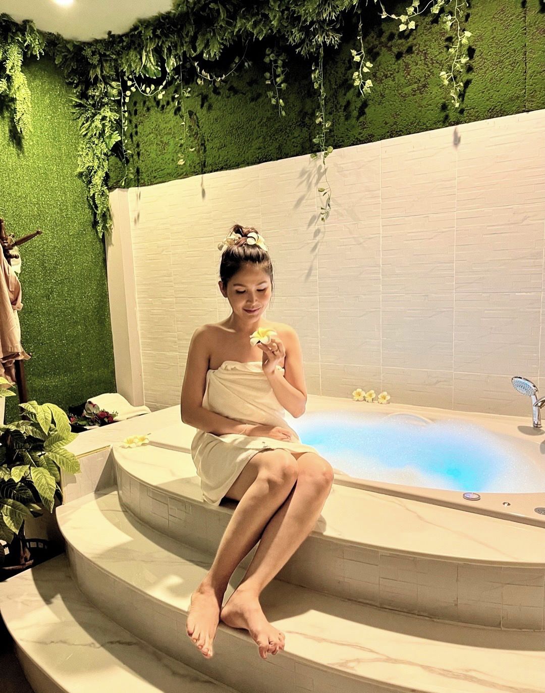 Eine Person sitzt in einer Badewanne vor einer grünen Wand und einem weißen Kachelboden.