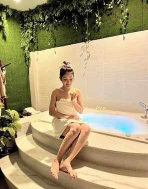 Una persona sentada en una bañera con una pared verde y un fondo de azulejos blancos.