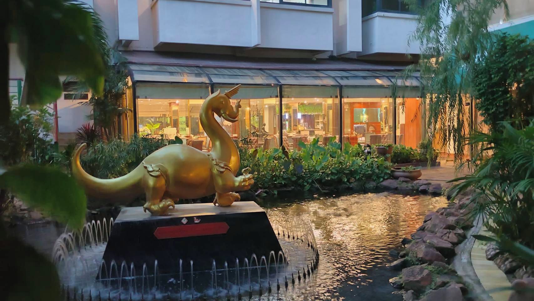 Una estàtua de dinosaure en una zona amb aigua, amb un edifici al fons.