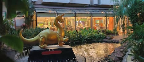 A dinosaur statue in a water feature with a building in the background.