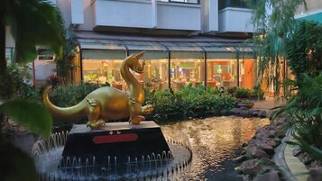 Una estatua de dinosaurio en una fuente acuática, con un edificio al fondo.