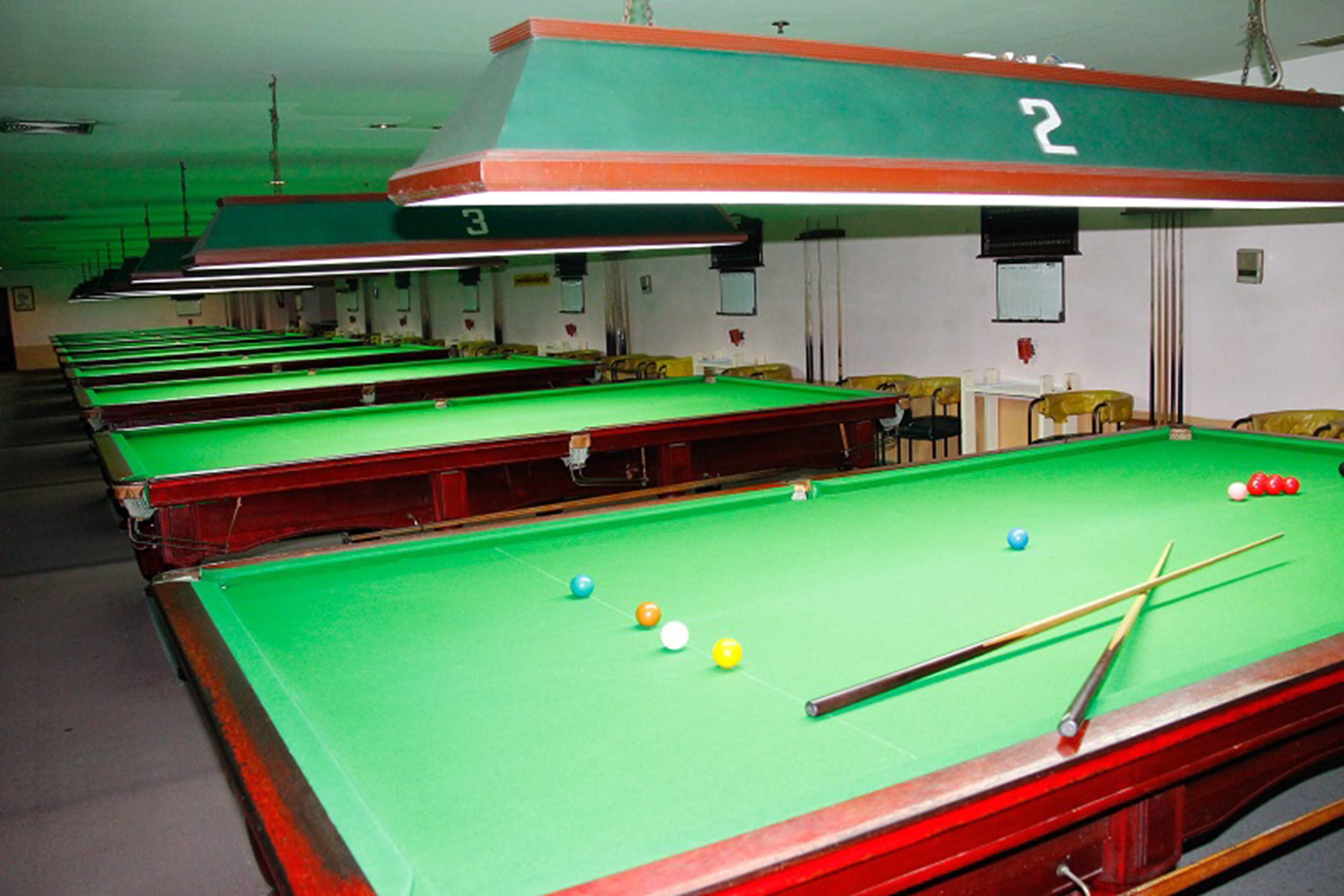 A pool hall with multiple tables and a green pool table with balls and a cue stick.