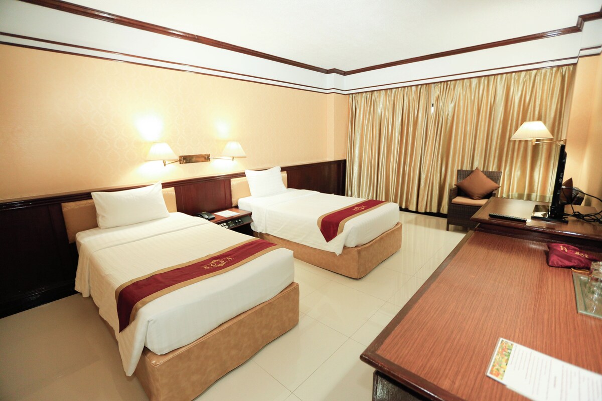 A hotel room with two beds, a desk, a chair, a lamp, and a curtain.
