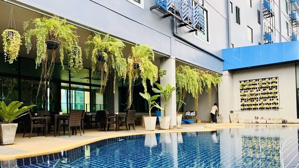 A swimming pool with hanging plants, outdoor seating, and a modern building facade. - Mantra Varee Hotel (Khon Kaen)