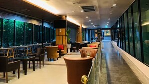 A modern hotel lobby with a long reception desk, comfortable seating areas, and large windows offering views of the outdoors. - Mantra Varee Hotel (Khon Kaen)
