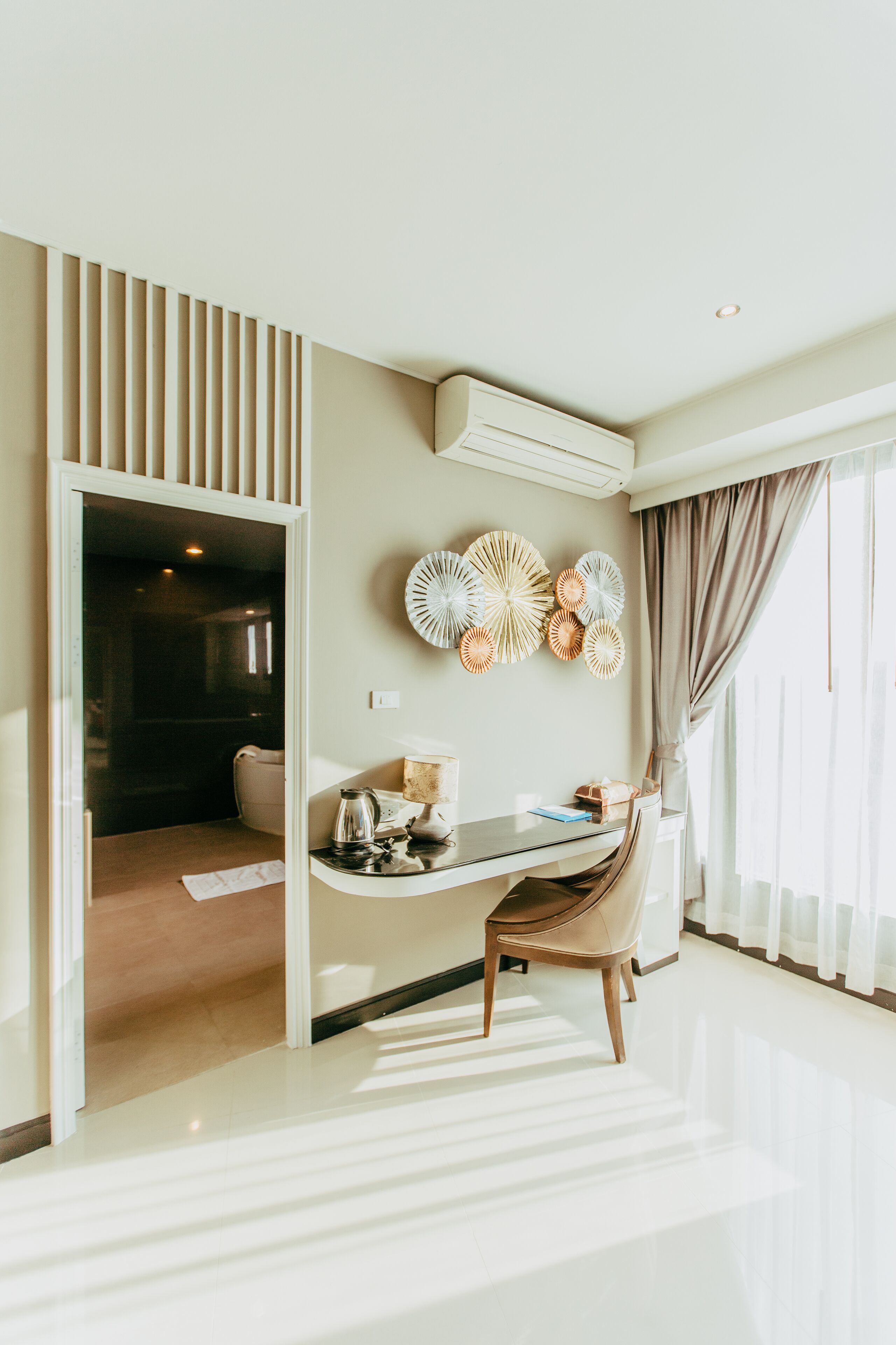 Une chambre d’hôtel moderne dotée d’un coin repas, d’une grande fenêtre avec des rideaux et d’un climatiseur fixé au mur.
