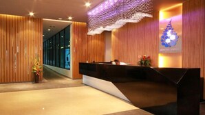 A reception area with a wooden reception desk, a decorative hanging light fixture, and a logo on the wall. - Mantra Varee Hotel (Khon Kaen)