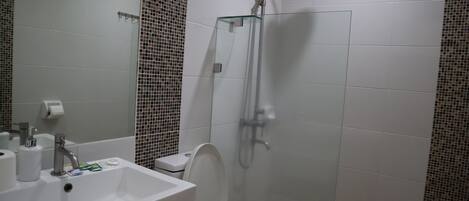 Ein modernes Badezimmer mit einer gläsernen Dusche, einem weißen Waschbecken und einer Toilette.