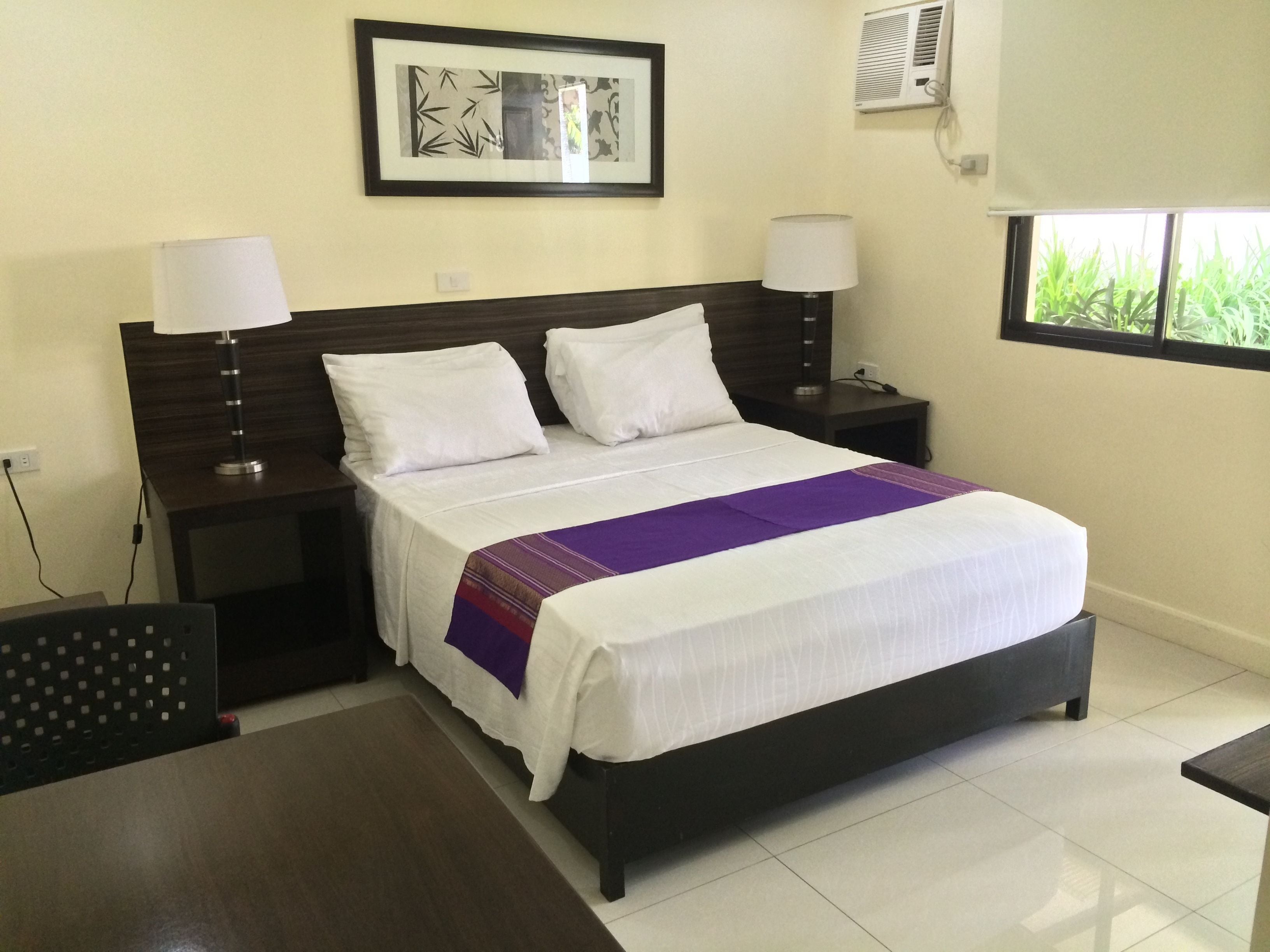 A neatly arranged hotel room with a large bed, two bedside tables, a desk, and a window with a view.