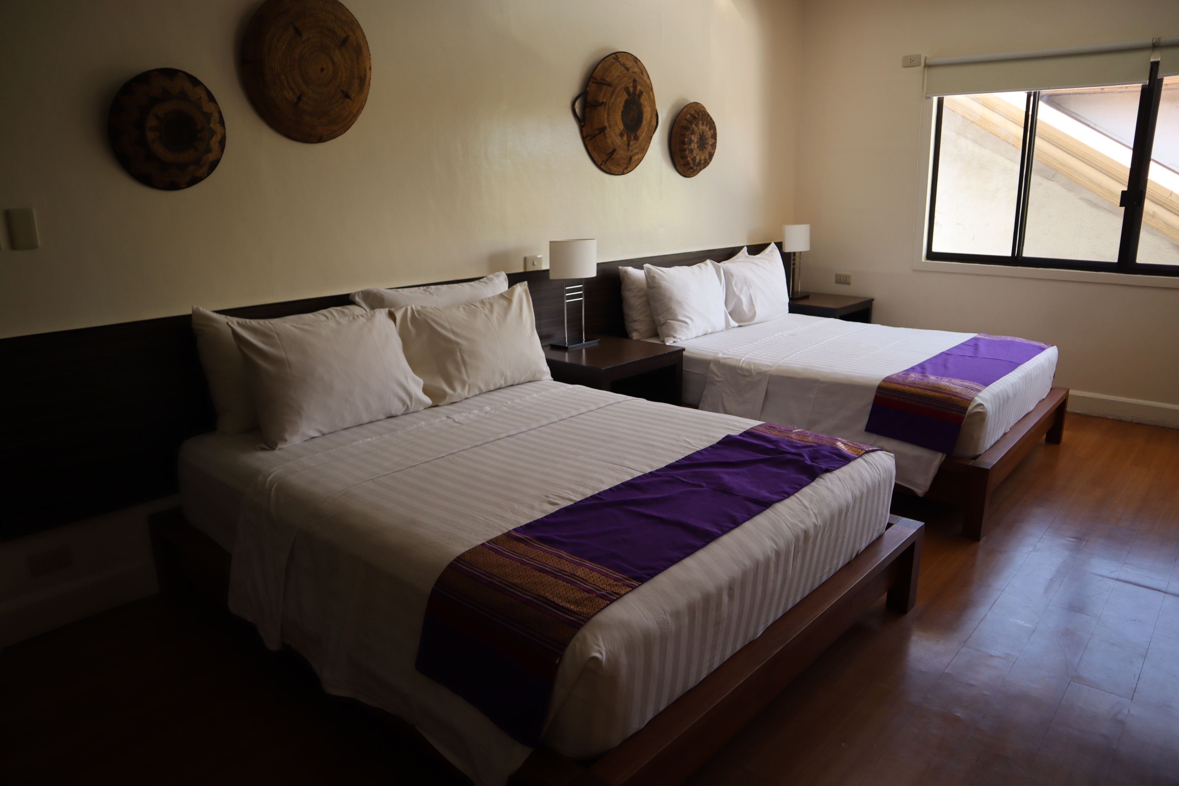 A hotel room with two beds, a wooden floor, and a window with a view.