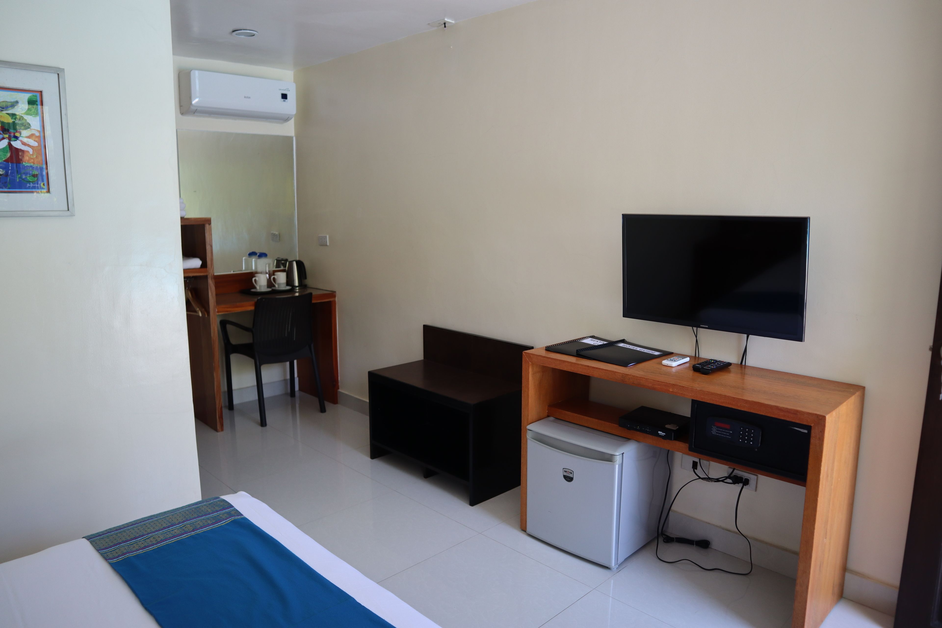 A hotel room with a bed, a desk with a computer, a television, and a small refrigerator.