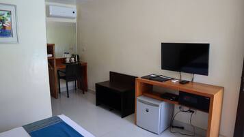 A hotel room with a bed, a desk with a computer, a television, and a small refrigerator.