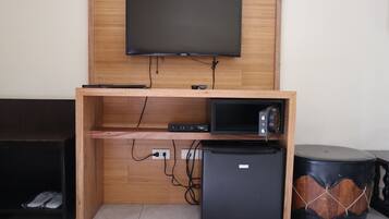 A wooden entertainment unit with a flat-screen TV, a small refrigerator, and a speaker.