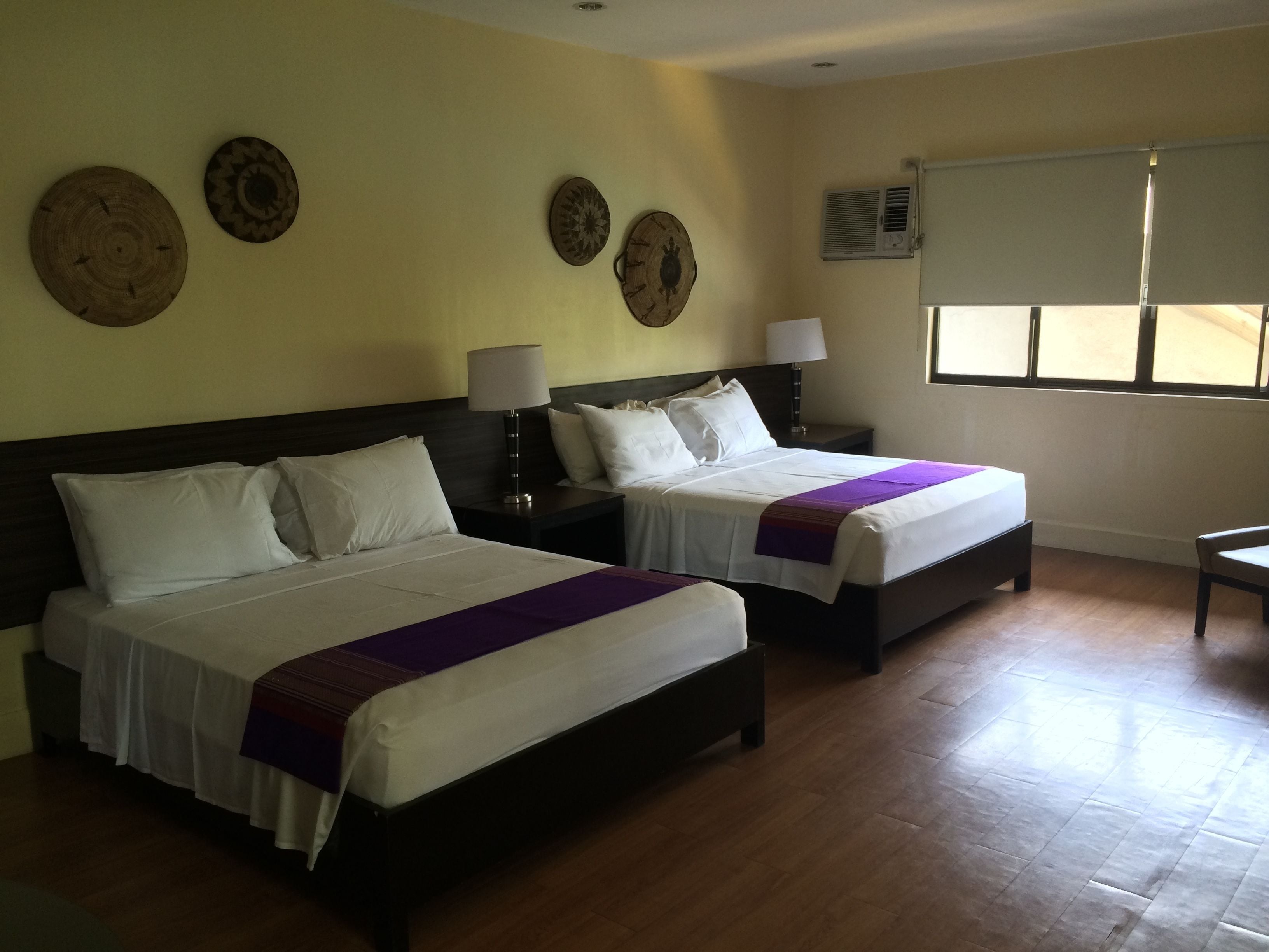 Habitación de hotel con dos camas, pisos de madera y paneles decorativos en la pared.