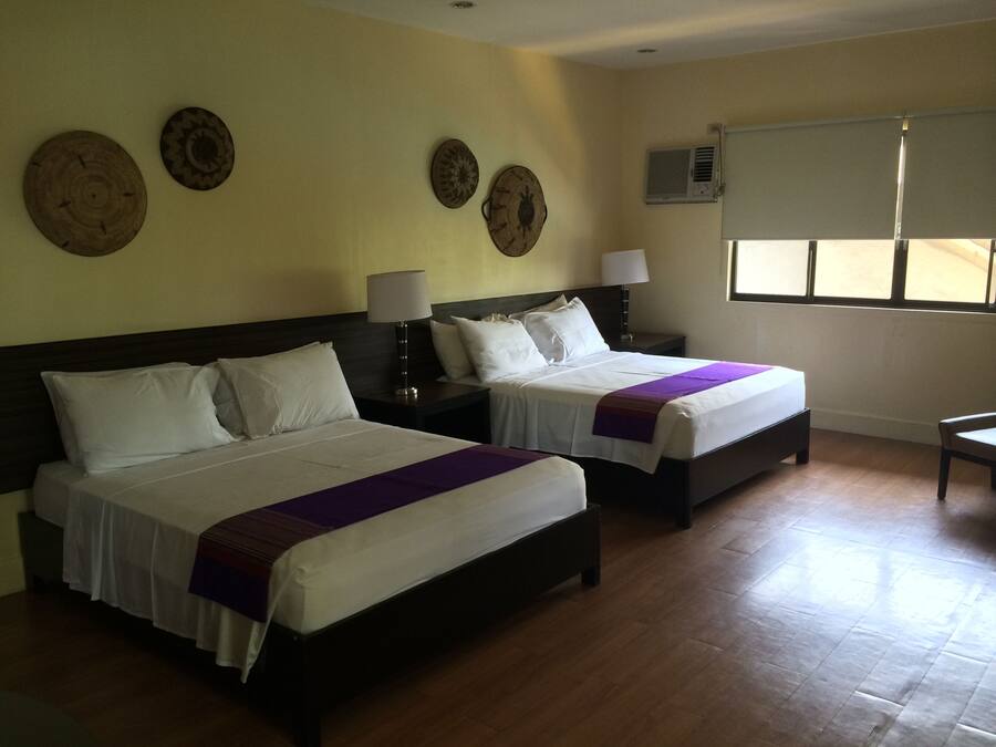 Habitación de hotel con dos camas, pisos de madera y paneles decorativos en la pared.