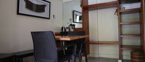 A room with a dining table, chairs, a framed artwork, a wardrobe, and a mirror.