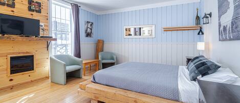 Una habitación con cama, televisión, sillón, mesa y chimenea.