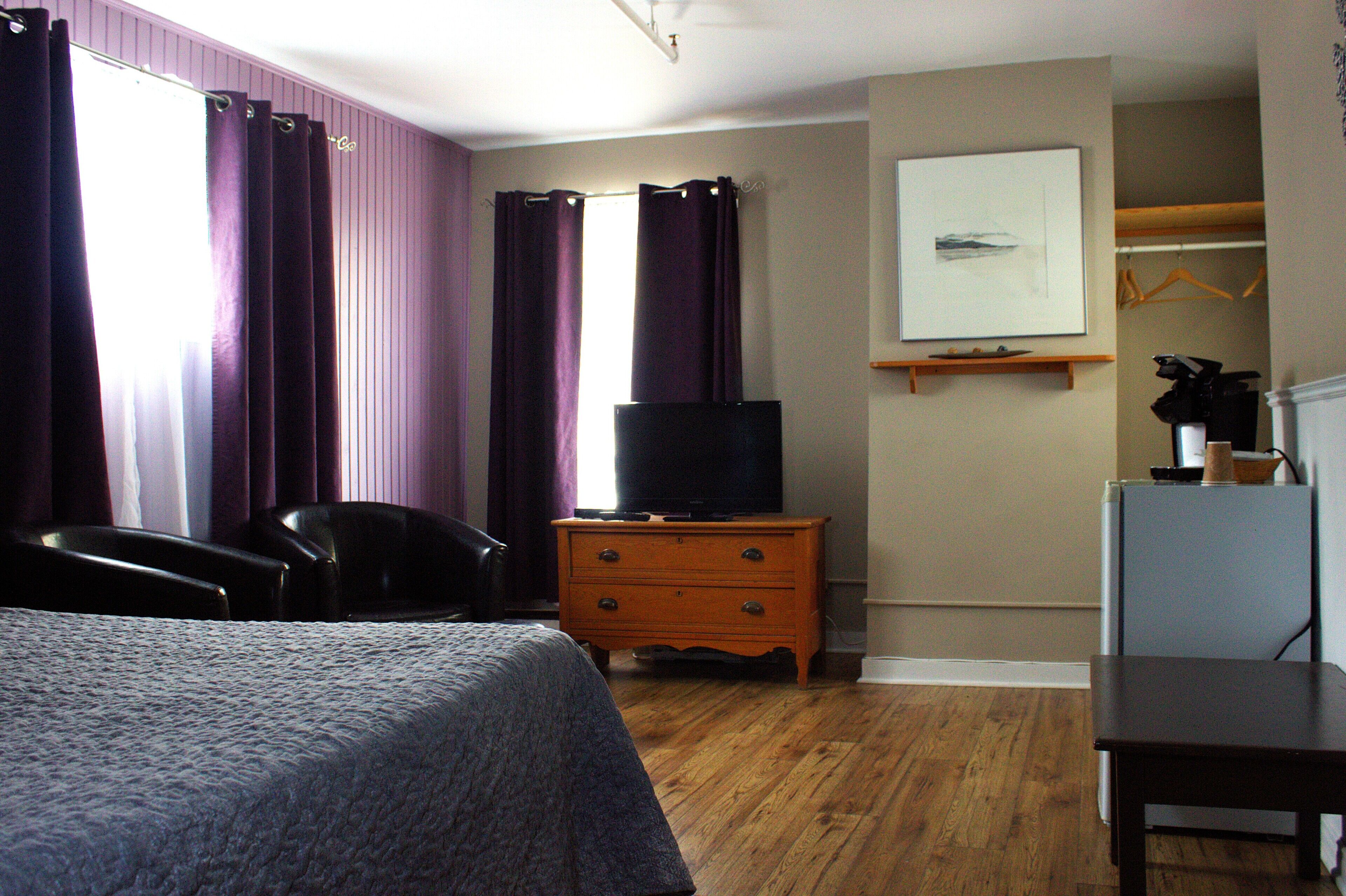 A hotel room with a bed, a dresser, a television, a chair, and a coat rack.