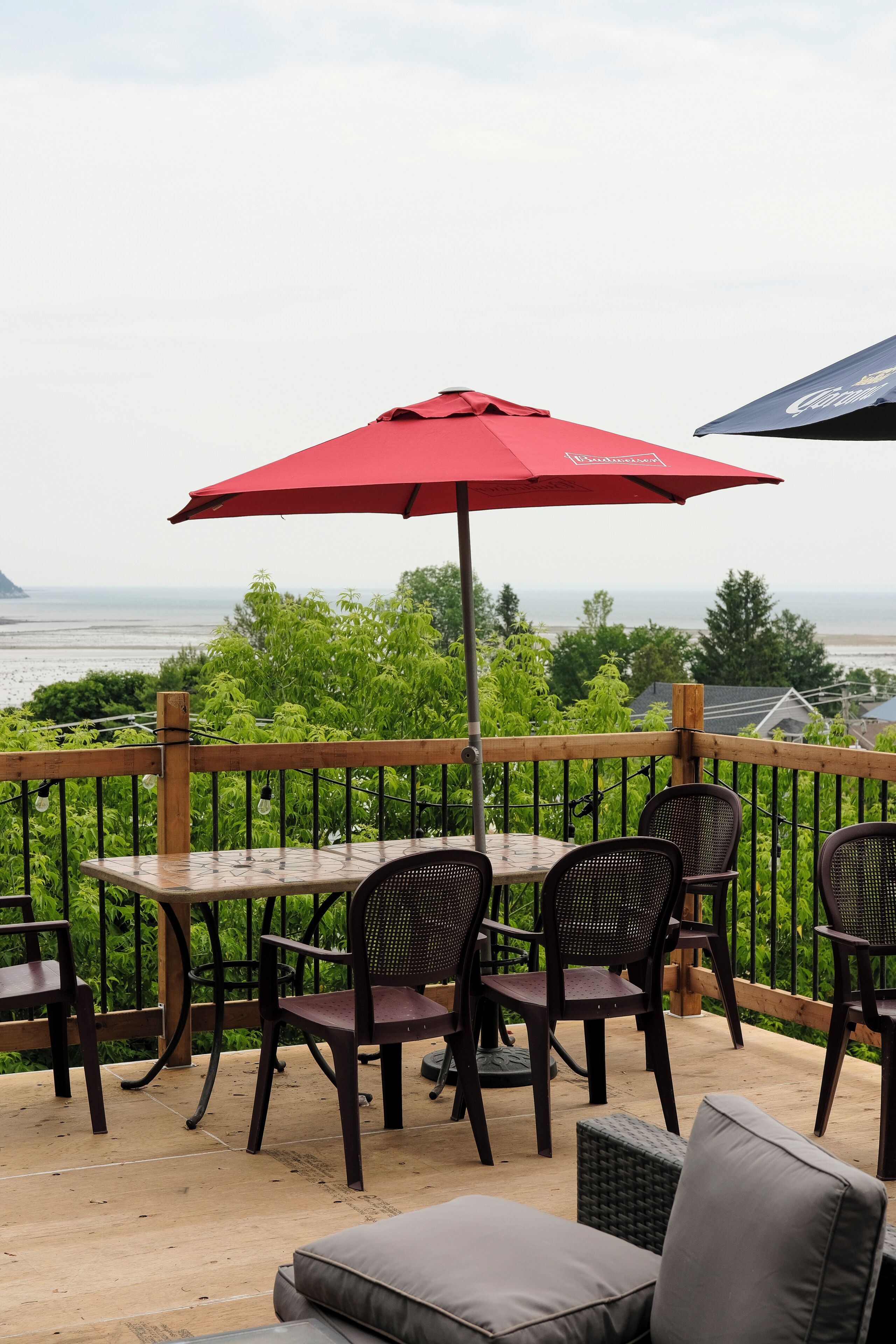 An outdoor patio with a table and chairs, a red umbrella, and a view of the sea.