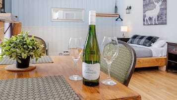 Een kamer met een eettafel, gedekt met wijnglazen en een fles wijn. Op tafel staat een bloempot, er is een bed met een dekbed en een wand met een ingelijste foto.