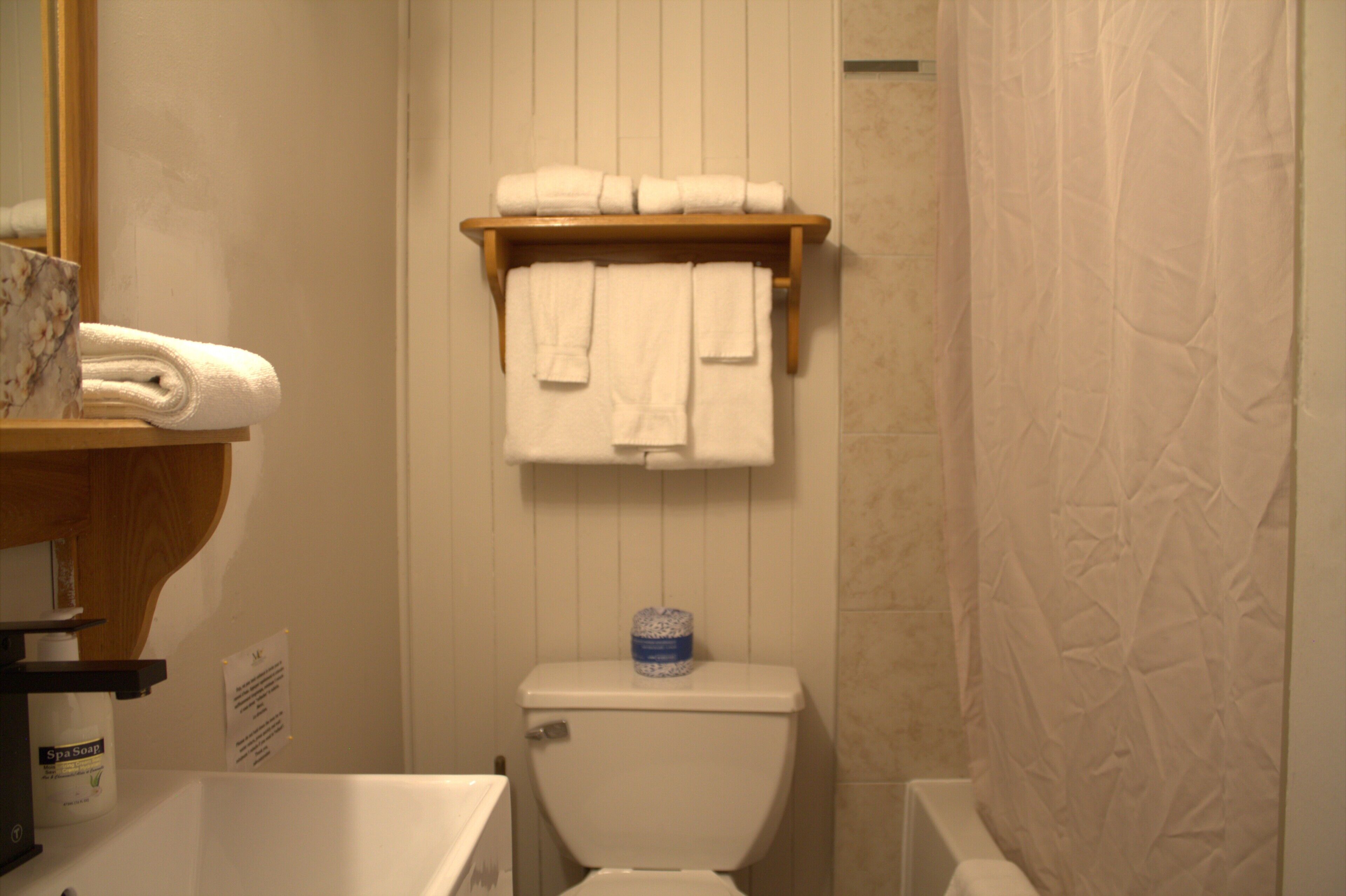 Un baño con inodoro, un estante con toallas dobladas y una cortina de ducha.