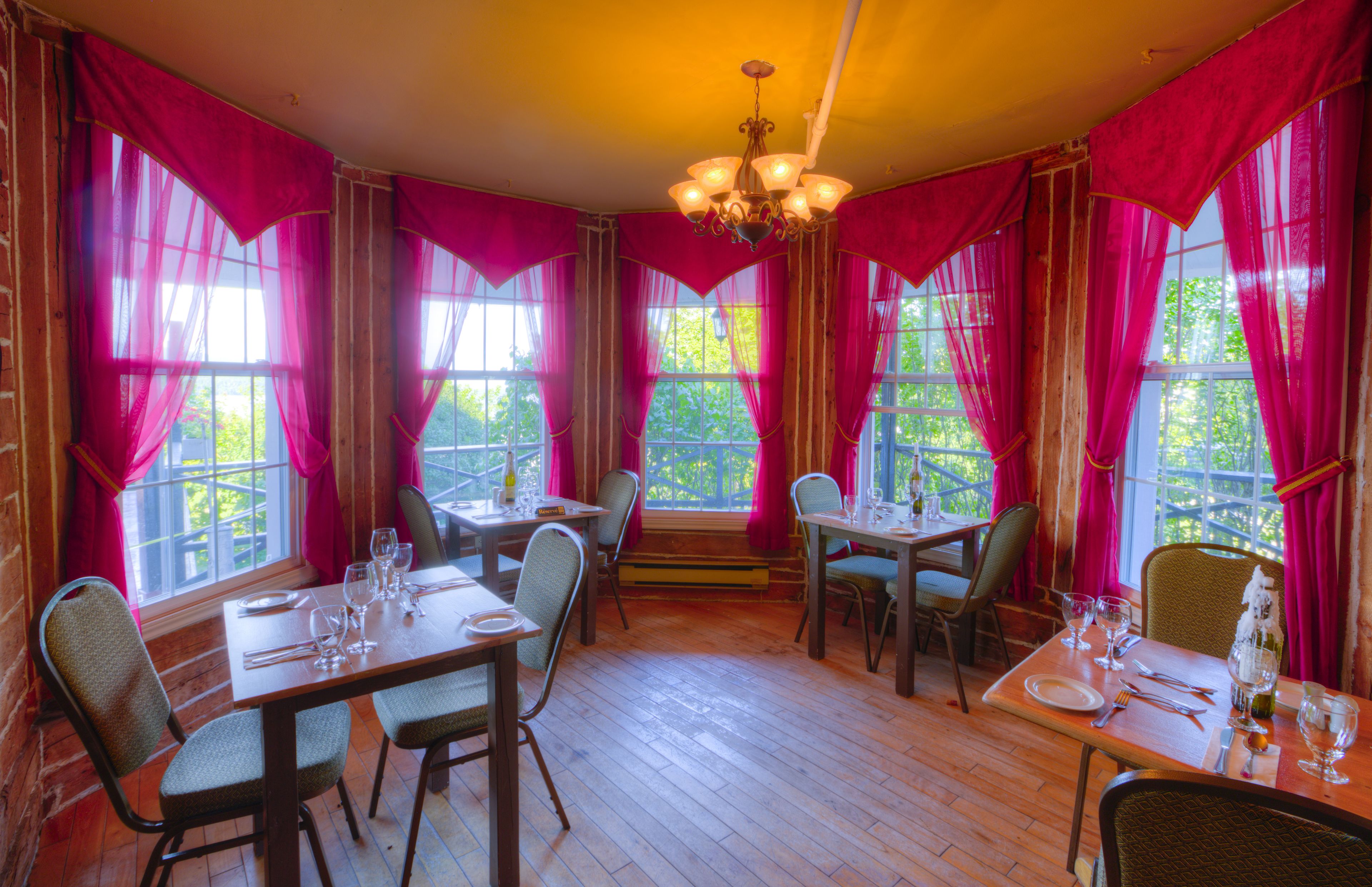 Uma sala de jantar com mesas e cadeiras de madeira, cortinas cor-de-rosa e um candelabro.