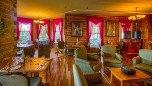 Un restaurante acogedor con paredes de madera, cortinas rojas y una combinación de zonas de comedor y descanso.