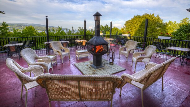 Un patio exterior con mobiliario de mimbre y una chimenea central, con vistas a un paisaje pintoresco.
