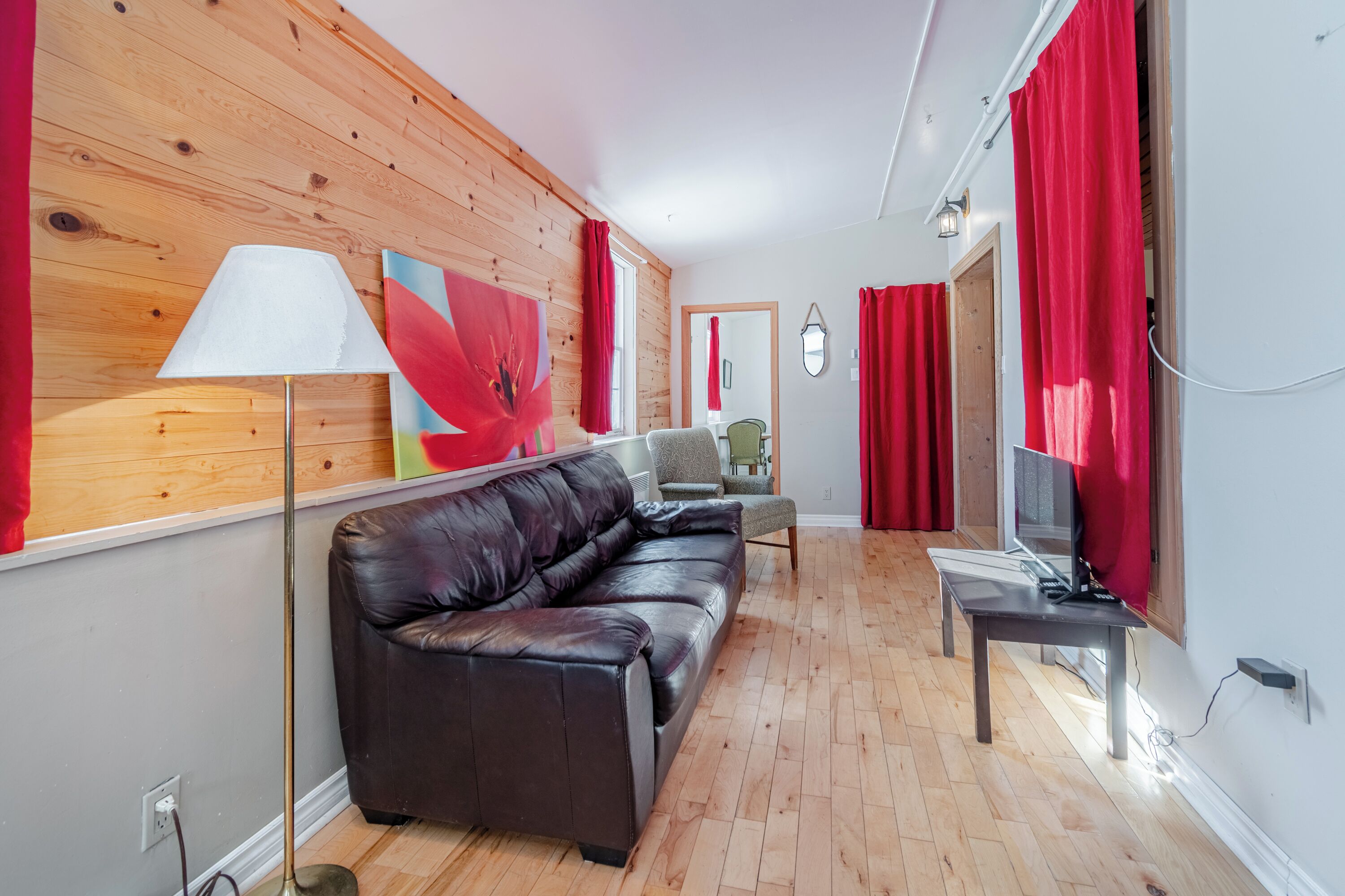 Un salón con un sofá de cuero, un televisor sobre un mueble bajo, piso de madera y una cortina roja.