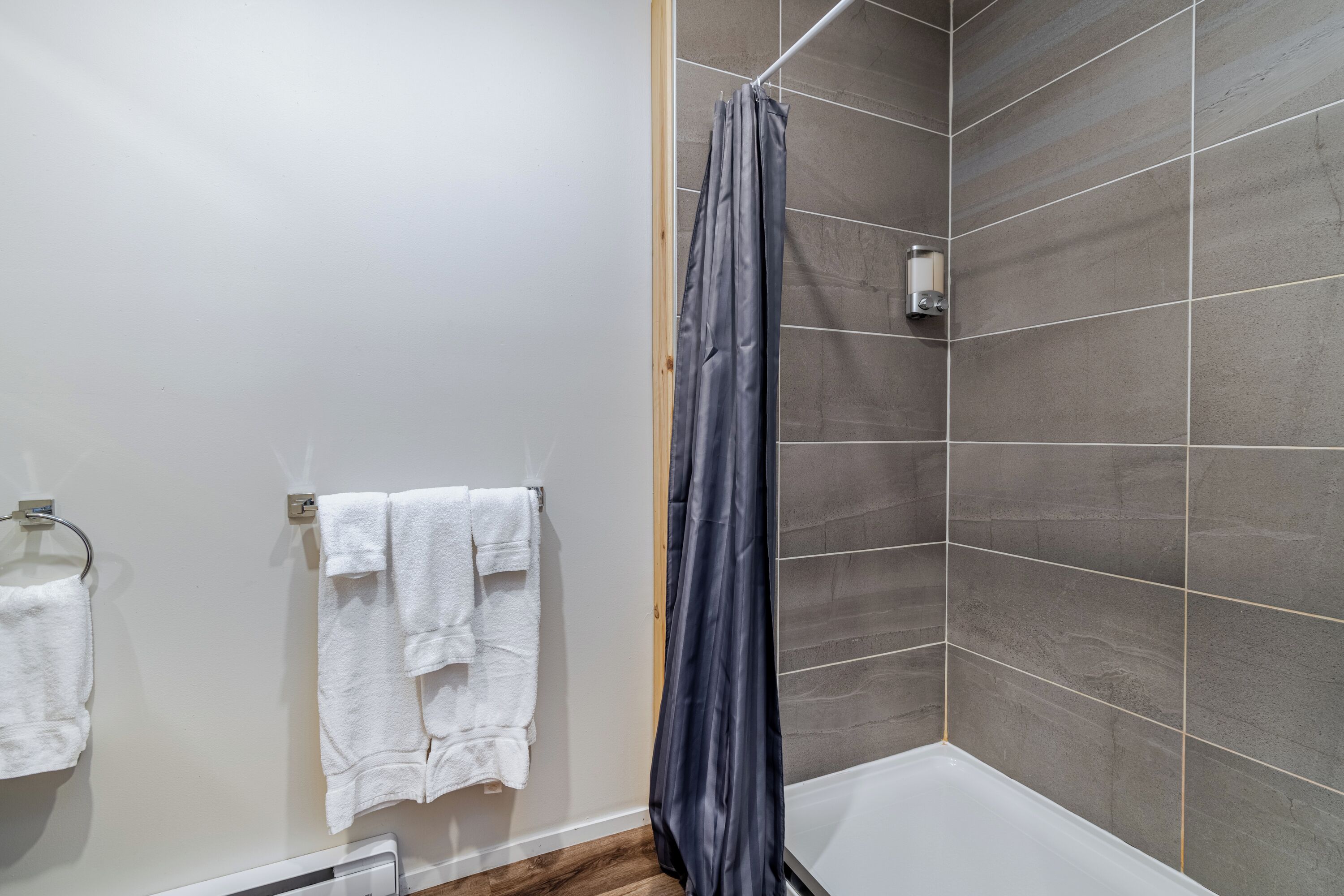 Un baño con ducha, un perchero con dos toallas y un dispensador de jabón en la pared.