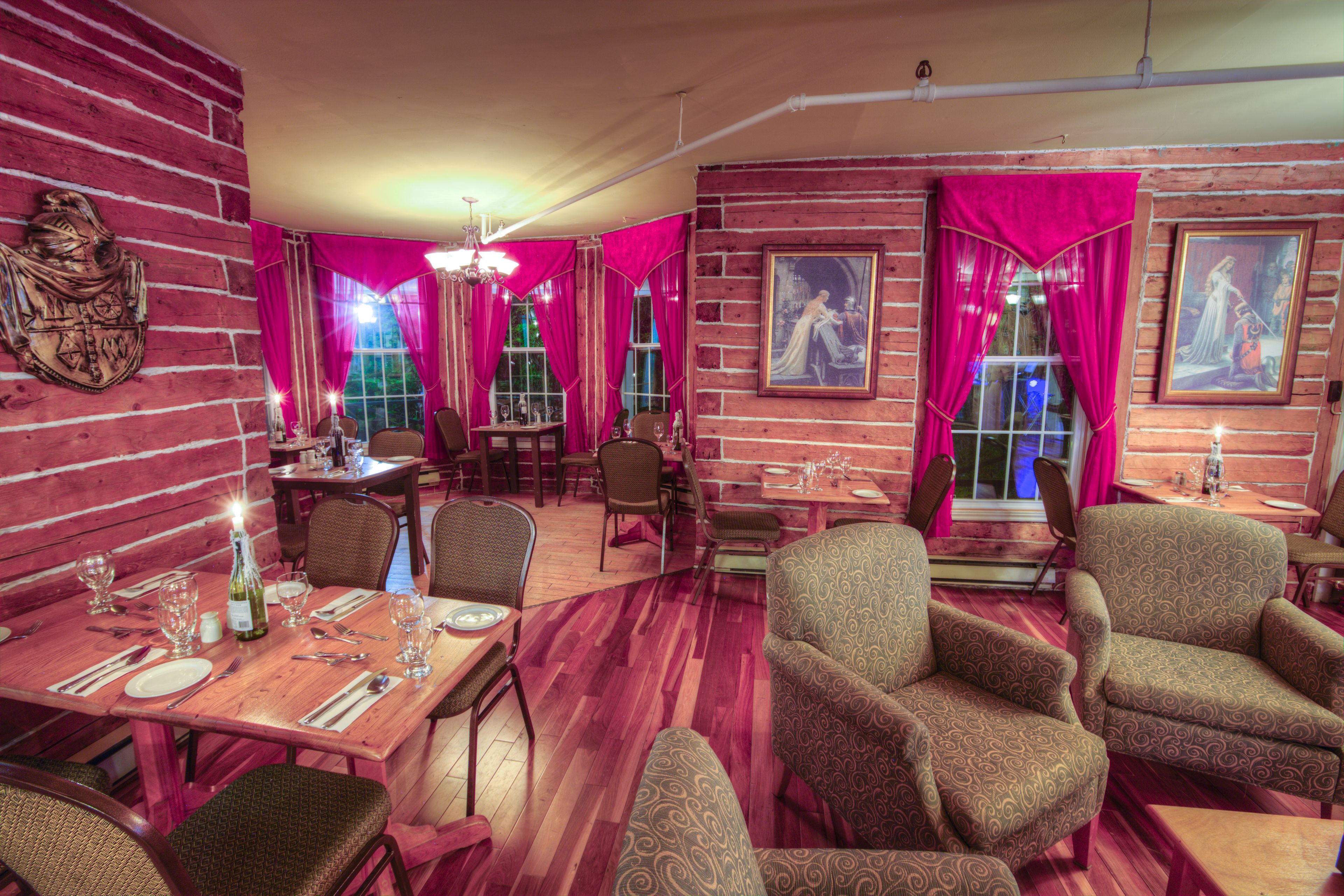 A restaurant with wooden walls, red curtains, and patterned chairs. Tables are set with wine glasses and cutlery.