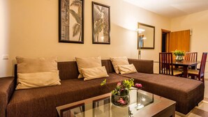 A living room with a sofa, a glass coffee table with a flower vase, and a dining area with a table and chairs. - VIP Executive Suites Maputo Hotel (Maputo)