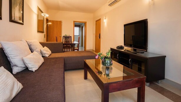 A modern living room with a sofa, a glass coffee table, a flat-screen TV, and a black entertainment unit. - VIP Executive Suites Maputo Hotel (Maputo)