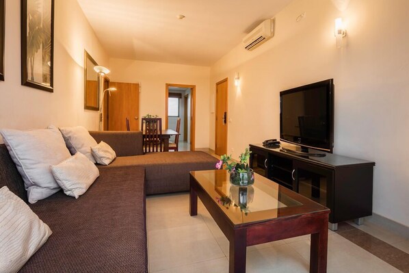 A modern living room with a sofa, a glass coffee table, a flat-screen TV, and a black entertainment unit.