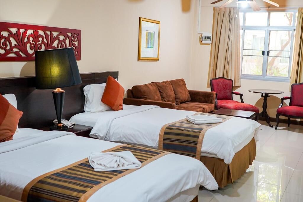 A hotel room with two beds, a sofa, a chair, a table, and a window with curtains.